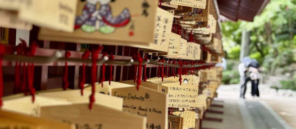 Plaquettes votives en bois suspendues à un cordon rouge dans un sanctuaire, couvertes de vœux écrits à la main en japonais.
